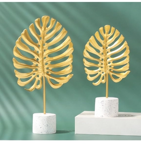Detailed close-up of golden metal monstera leaves on cylindrical terrazzo bases