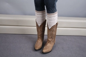 Détail de jambières en tricot avec texture ondulée portées sur un jean et des bottes