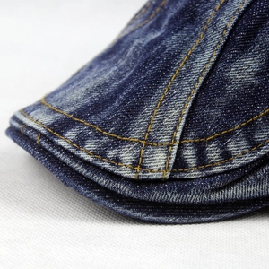 Close-up of dark blue denim flat cap showing yellow double-row stitching and washed texture