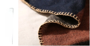 Macro shot of handmade stitching on color-block knit shawl with blue and tan details