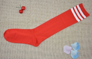 Detailed view of red cotton knee high socks with white triple stripes on a rustic mat