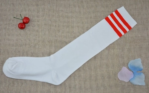 Flat lay of white knee-high sports socks with three red stripes on burlap with cherry decor