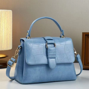 Detail of light blue crocodile-embossed handbag with gold-tone hardware and handle