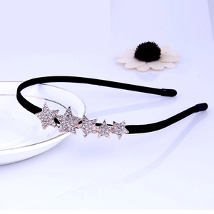 Detail of a thin black headband featuring five sparkling rhinestone stars on a tray