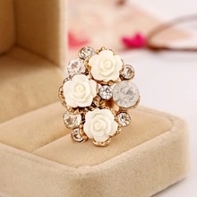 Gros plan d'une bague dorée ornée de roses en résine blanche et de strass brillants