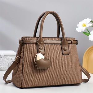 Brown woven texture tote bag with heart charm and detachable strap on studio background