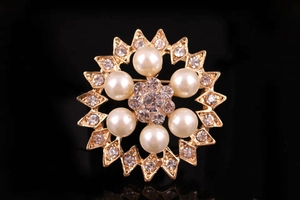 Dettaglio di una spilla a corona dorata con perle bianche e strass di cristallo