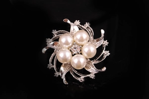 Dettaglio macro di una spilla floreale argento con perle e centro in strass scintillante
