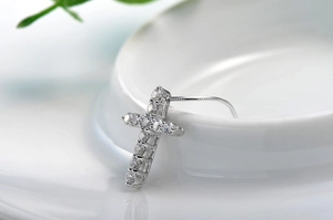 Macro shot of silver cross earring with sparkling diamonds on a minimalist background