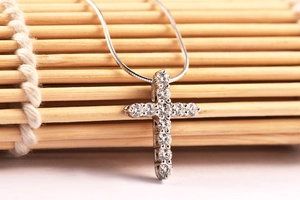 Close-up of a silver cross pendant with diamonds on a textured bamboo background