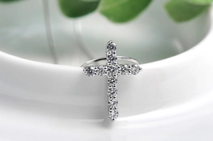 Close-up of silver cross earring with clear stones on a white ceramic surface