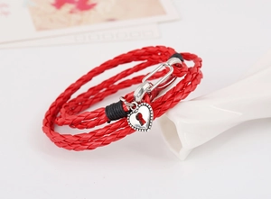 Detail of red braided leather bracelet featuring a silver heart lock and metal clasp
