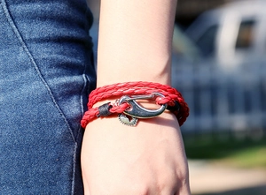 Detail of red woven leather wrap bracelet featuring a silver heart charm on wrist