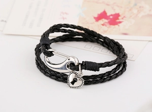 Detail of multi-layer black braided leather bracelet with heart lock charm and silver clasp
