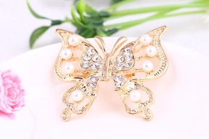 Detail of a gold butterfly brooch featuring hollow patterns, pearls, and rhinestones
