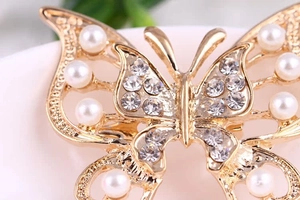 Macro shot of gold butterfly brooch featuring hollow design with pearls and rhinestones