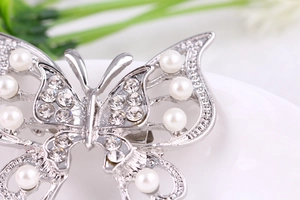 Macro detail of silver butterfly brooch featuring hollow wings with pearls and rhinestones