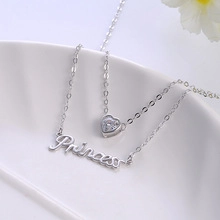 Close-up of double-layer silver necklace with heart pendant and Princess script charm