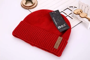 Detailed view of a red knitted beanie with a folded cuff and leather patch accent