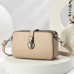 Detail of beige litchi grain leather crossbody bag with three zippers and metal buckle