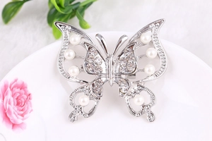 Detailed view of large hollow butterfly brooch with pearls and rhinestones on a ceramic tray