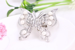 Detail of silver hollow butterfly brooch with pearls and rhinestones on a ceramic plate