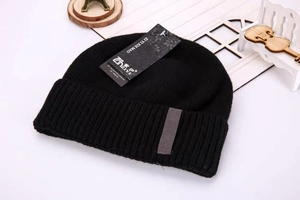 Detail of black knitted beanie featuring thick ribbed texture and grey leather brand patch