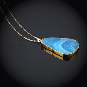 Macro view of blue irregular crystal pendant with gold edge on dark mirror background