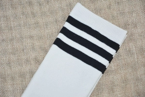 Close-up of white knee-high socks with black triple stripes on beige linen background
