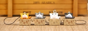 Set of four 3D cartoon cat charms in boxes with lanyards on a warm wood background