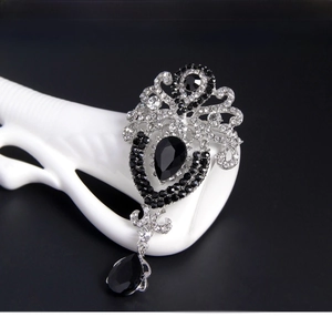 Detail of vintage crown brooch with black teardrop gems and crystals on a white hand stand