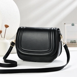 Classic black saddle bag with decorative trim and gold hardware in a minimalist setting