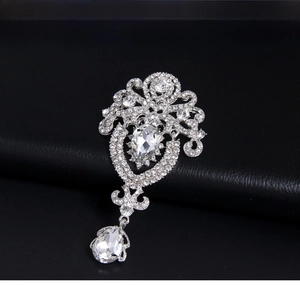 Close-up of a silver baroque crown brooch with white rhinestones and a crystal drop
