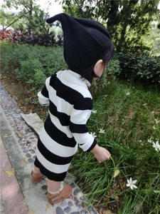 Detail of child wearing a striped knit dress with a black pointed beanie hat outdoors