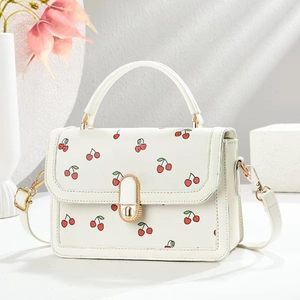 Close-up of white crossbody bag with cherry prints and elegant gold metal buckles