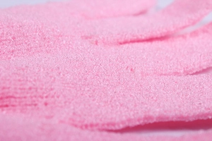 Macro detail of pink exfoliating bath glove showing textured nylon scrubbing fabric
