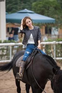 Chic women's black leather jacket with metal zippers shown in a stylish equestrian setting