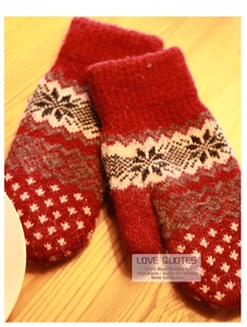 Close-up of red thick knit mittens with white snowflake patterns on a wooden surface