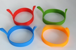 Overhead view of four colorful round silicone egg rings with double safety handles