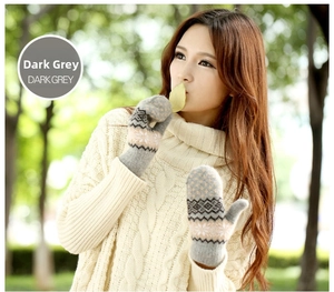 Close-up of thick dark grey knitted mittens featuring white snowflake patterns and geometric motifs