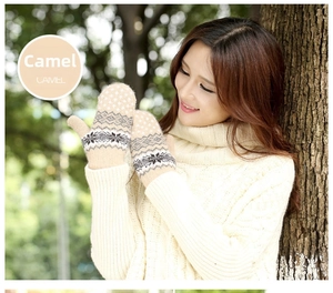 Close-up of camel knit mittens with white snowflake patterns in an outdoor winter setting