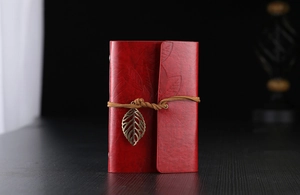 Detail of dark red vintage leather notebook with leaf embossing and bronze metal pendant