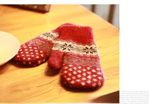 Detail of red knit mittens with white snowflake patterns on a rustic wooden surface