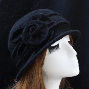 Detail of elegant black wool cloche hat featuring a decorative side flower on a model