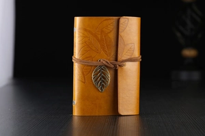 Macro detail of leaf embossed leather cover with bronze metal leaf pendant charm