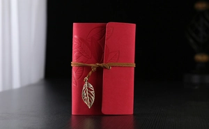 Detailed view of the red faux-leather journal with embossed leaf and metal pendant