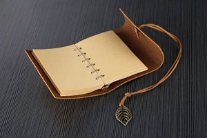 Close-up of small vintage leather notebook with bronze leaf pendant and tie closure