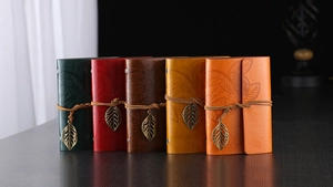 Detail of five vintage leather notebooks with leaf pendants and strap closures on wood