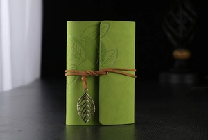 Detailed view of green leather notebook featuring leaf embossing and a bronze leaf pendant
