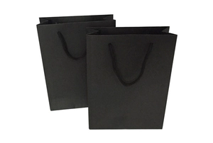 Detail of minimalist black paper gift bag with matching woven rope handles and matte texture